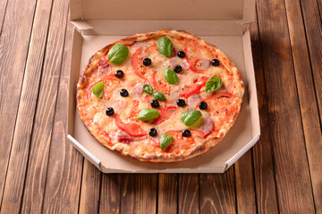 Carton box with delicious pizza on wooden background