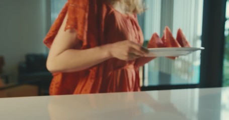 Young woman picking up watermelon in kitchen and going to balcony