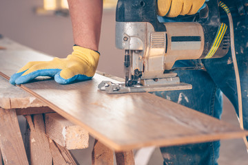 The worker cuts boards with an electric jigsaw, dust flies in all directions, carpentry