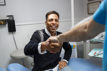 Young African-American man shaking hand of crop dentist having visit in medical clinic. 