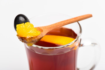 Healing drink concept. Glass with mulled wine with spoon full of honey. Glass with mulled wine or hot tea with grape, cinnamon and honey on white background, close up. Drink with slice of orange