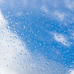 Rain drops on a window pane, background sky and clouds, square