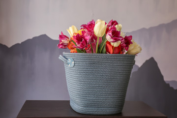 Basket with beautiful tulips on table against color background