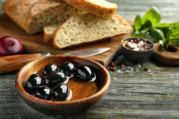 Bowl with black olives and oil on wooden table