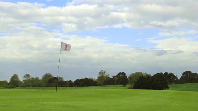 Green golf course with white flag and the hole. Sport, relax, recreation and leisure concept. Summer landscape on a bright sunny day with cloudy sky