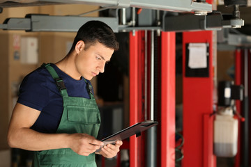 Young auto mechanic with clipboard near car in service center