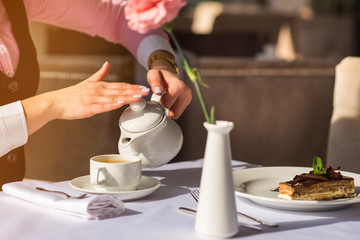Woman have breakfast and pours tea from teapot into the cup in the morning