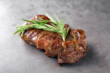 Tasty grilled steak with rosemary on grey background