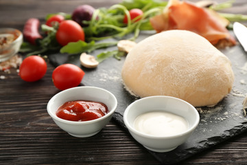 Raw dough and ingredients for pizza on wooden background