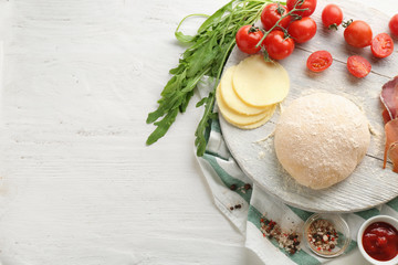 Composition with raw dough and ingredients for pizza on wooden background