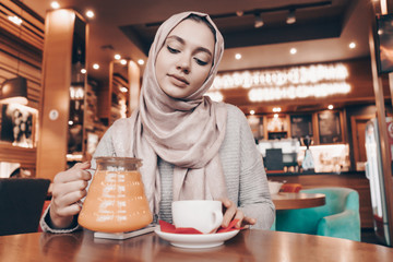 an attractive Arab girl with a headscarf on her head dines in a cozy restaurant, drinks tea