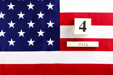 Straightened American flag and wooden cube calendar with 4th of July, USA Independence Day date, copy space celebratory background. US patriotic festive composition, top view, close up.