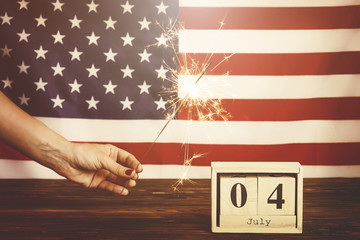 Retro toned cropped shot, woman holding burning sparkler, bengal light on American flag background....
