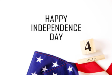Ruffled American flag and wooden cube calendar with 4th of July congratulations. Happy Independence Day greeting card text on white copy space background. Patriotic composition, top view, close up.