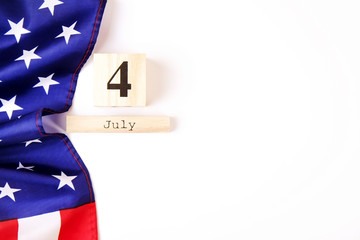 Ruffled American flag and wooden cube calendar with 4th of July date. Happy Independence Day greeting card template on white copy space background. US patriotic festive composition, top view, close up