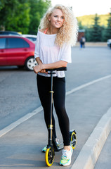 Full-length photo of curly-haired athletic woman kicking on scooter in park