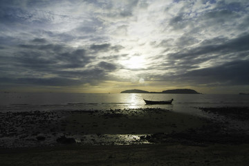 Boat float in the sea near beach in early morning and the Sun is growing up which has overlay clouds, dim light image