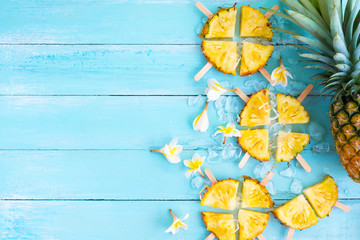 Pineapple popsicle sticks with ice on wood plank blue color. summer fruit concept, top view