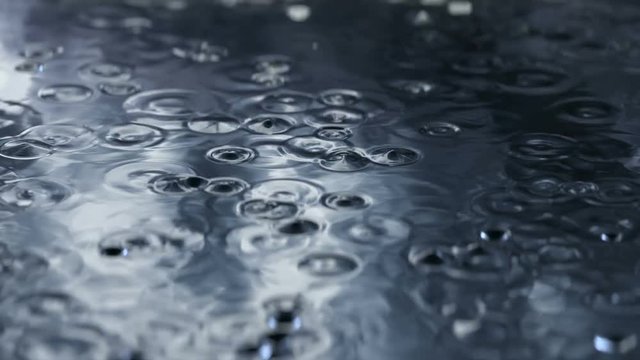3D animation of the rain drops rippling in a street puddle with reflections of the dark stormy sky