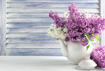 Vase with beautiful blossoming lilac on table against wooden background