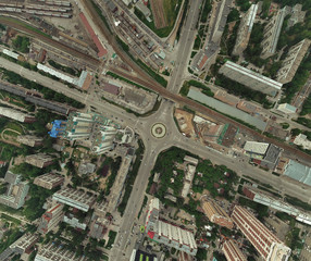 Aerial view of square in the city with roundabout traffic, streets and buildings with green trees and railway station