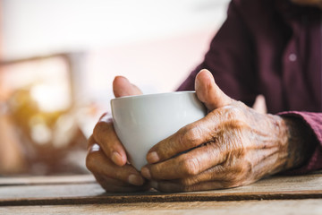 Hands of old man holding cup of coffee on the wood table.vintage tone