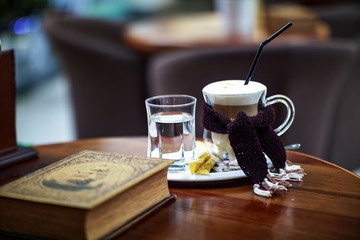 hot latte in a glass cup, stands on a table next to a book and decorations, in a mall in a cafe