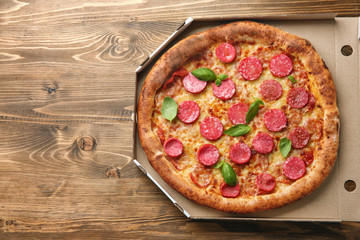 Carton box with delicious pizza on wooden background