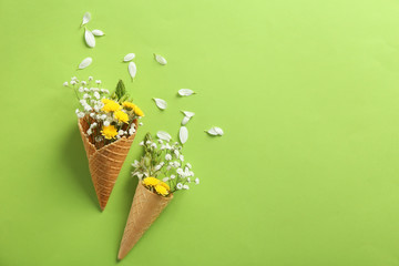 Waffle cones with beautiful flowers on color background