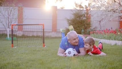 Old man with his grandson are playing football at the backyard