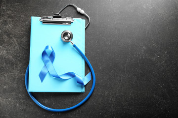 Blue ribbon, stethoscope and clipboard on dark background. Prostate cancer concept