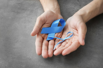 Male hands holding blue ribbons on grey background. Prostate cancer concept