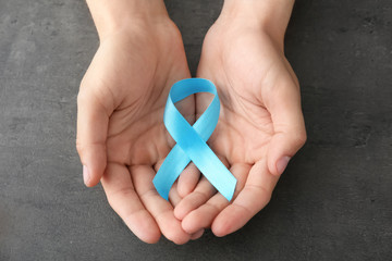 Male hands holding blue ribbon on grey background. Prostate cancer concept