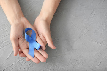 Male hands holding blue ribbon on grey background. Prostate cancer concept