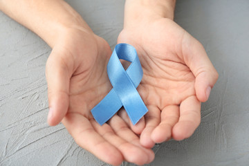 Male hands holding blue ribbon on grey background. Prostate cancer concept