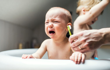 An unhappy baby girl with unrecognizable father crying when brushing teeth.