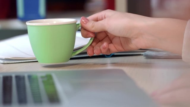 Business woman drink coffee in office. Close up of woman hand holding green coffee cup on desk. Corporate business office lifestyle. Coffee break and relaxing on workplace. Female hand hold cup of tea
