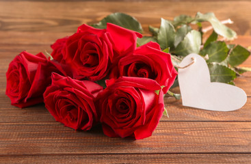 Beautiful roses with heart-shaped tag on wooden background