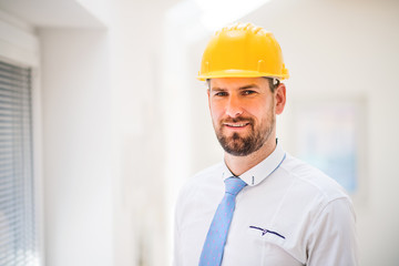 A young engineer or architect with white shirt, tie and helmet in a room.