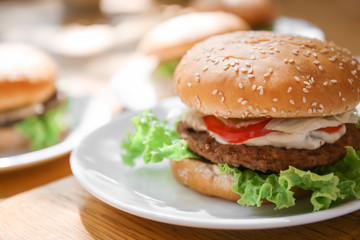 Plate with tasty cheeseburger on table