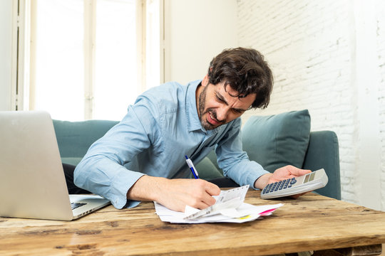 Angry Man Paying Bills As Home With Laptop And Calculator