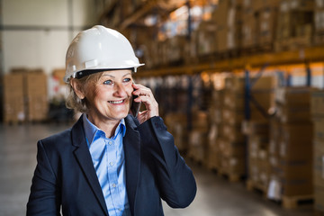 Senior woman warehouse manager or supervisor with smartphone.