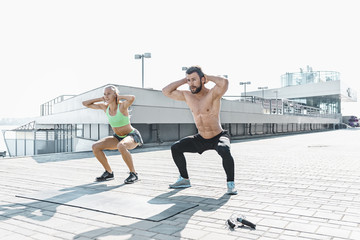 Fit fitness woman and man doing fitness exercises outdoors at city