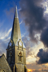 Church steeple with clock faces on each side beneath dramatic early evening sky.