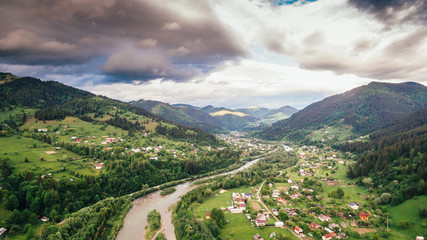 Fototapeta na wymiar Aerial View: Carpathian village is located in the valley of wooded mountains