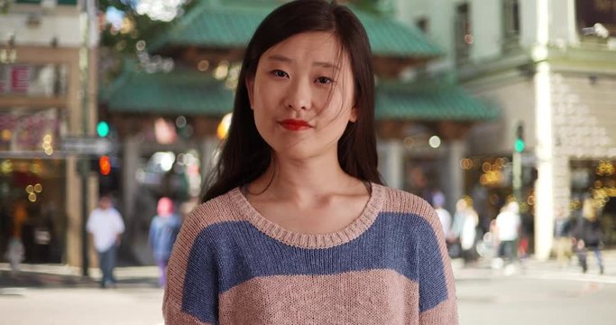 Casual millennial woman looking at camera with blank expression and wearing a sweater in Chinatown, Close-up of Asian female in static pose in San Francisco looking to side, 4k