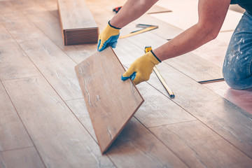 Professional installation of floor covering, the worker quickly and qualitatively mounts a laminate board - obrazy, fototapety, plakaty