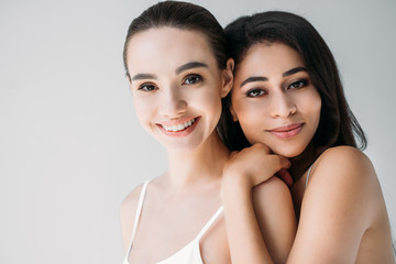portrait of smiling multicultural women looking at camera isolated on gray background