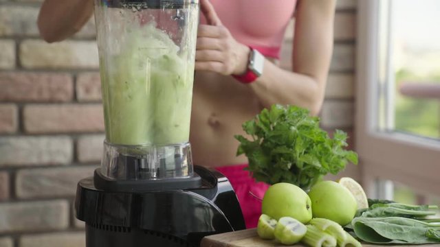 Slim sporty woman making a homemade green detox smoothie
