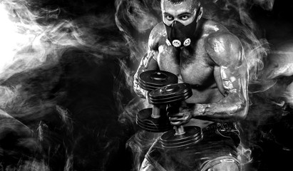 Muscular young fitness sports man in training mask. Workout with dumbbell in fitness gym